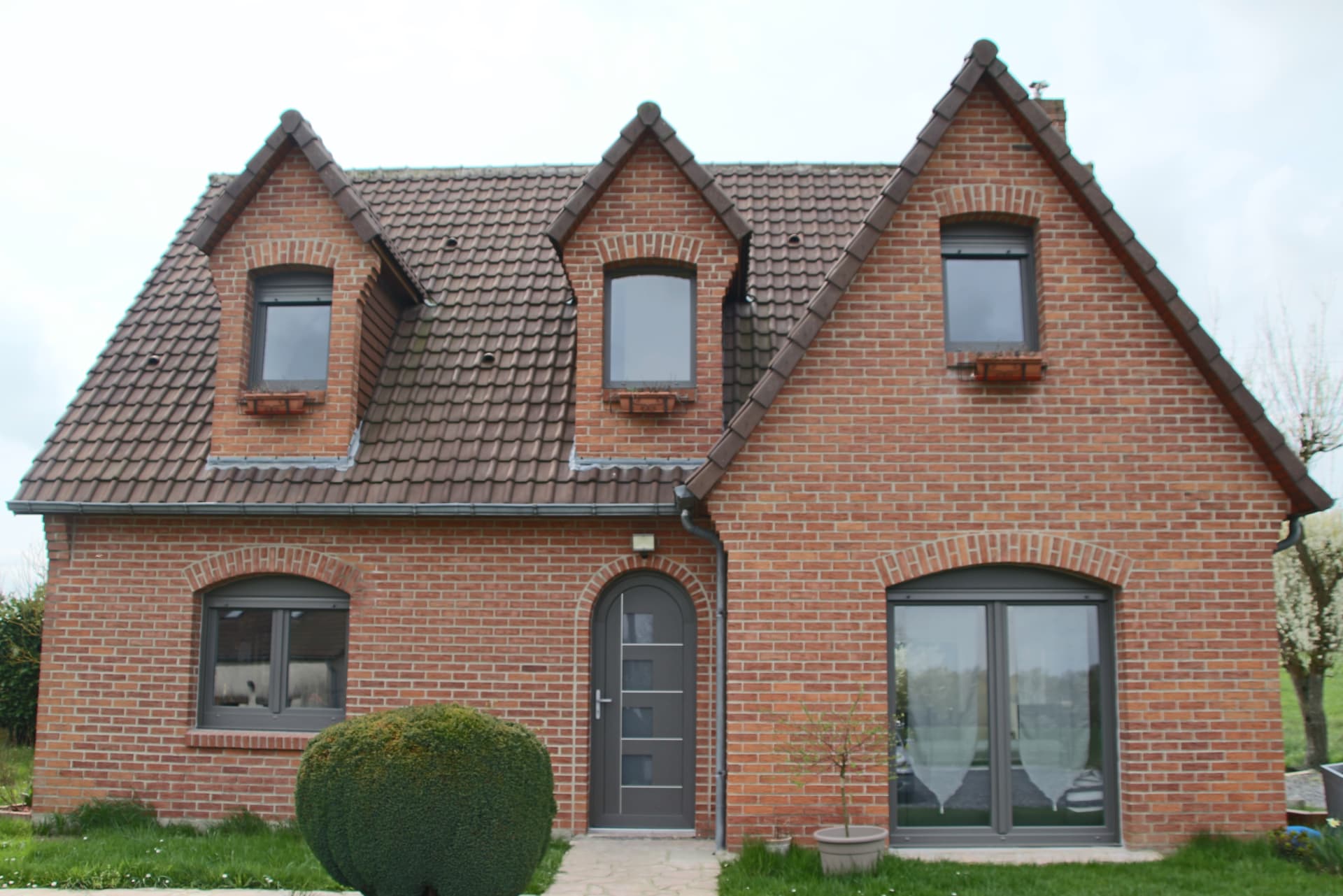 Maison en brique avec fenêtres cintrées et porte aluminium gris