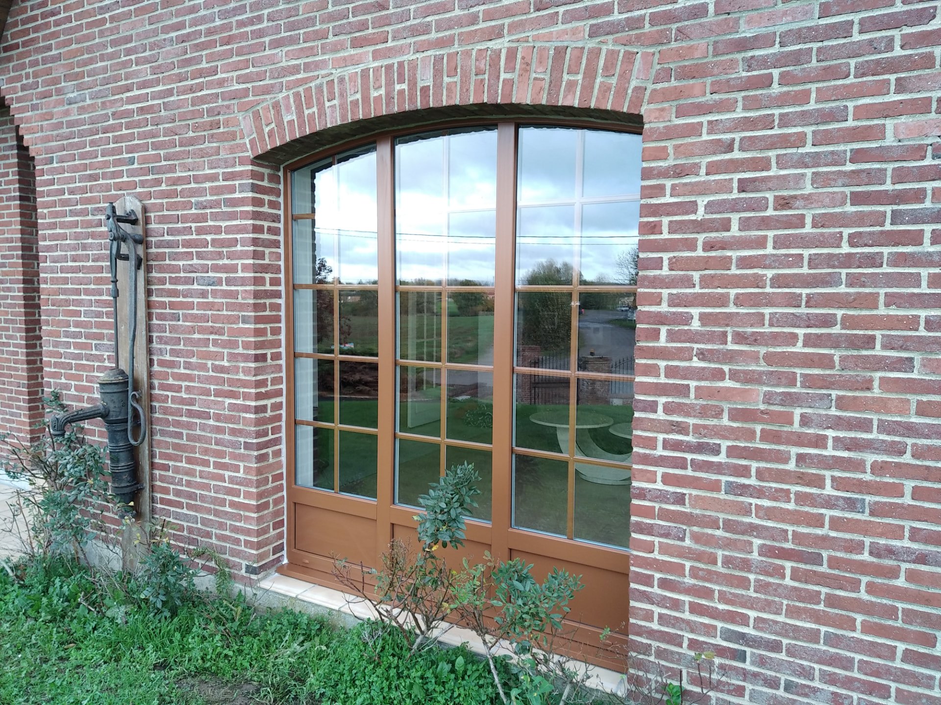 Baie cintrée à petits bois teinte chêne doré dans une façade en brique