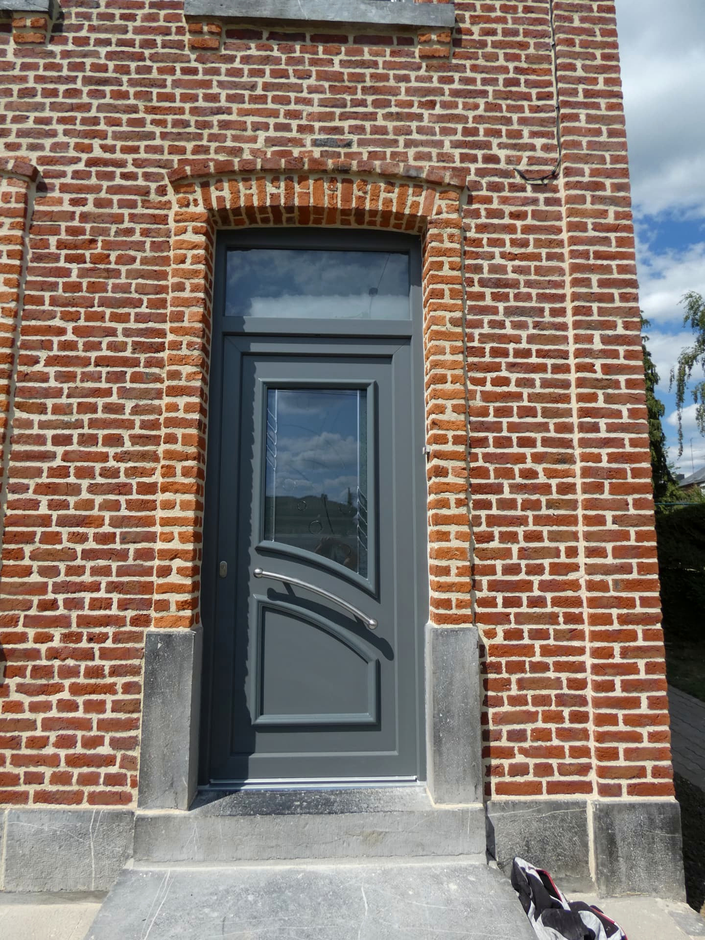 Réalisation VITREC d'une porte d'entrée grise avec vitrage courbe et imposte vitrée sur façade en briques