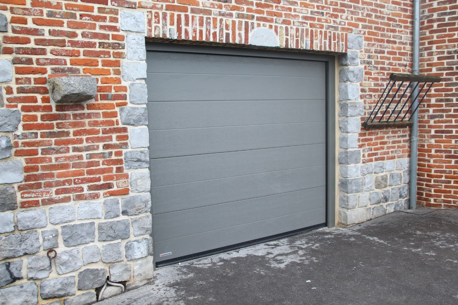 Porte sectionnelle grise sur façade en briques et pierre