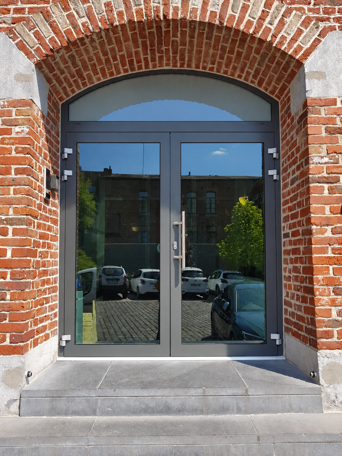 Double porte vitrée aluminium anthracite avec imposte cintrée sous arche en brique