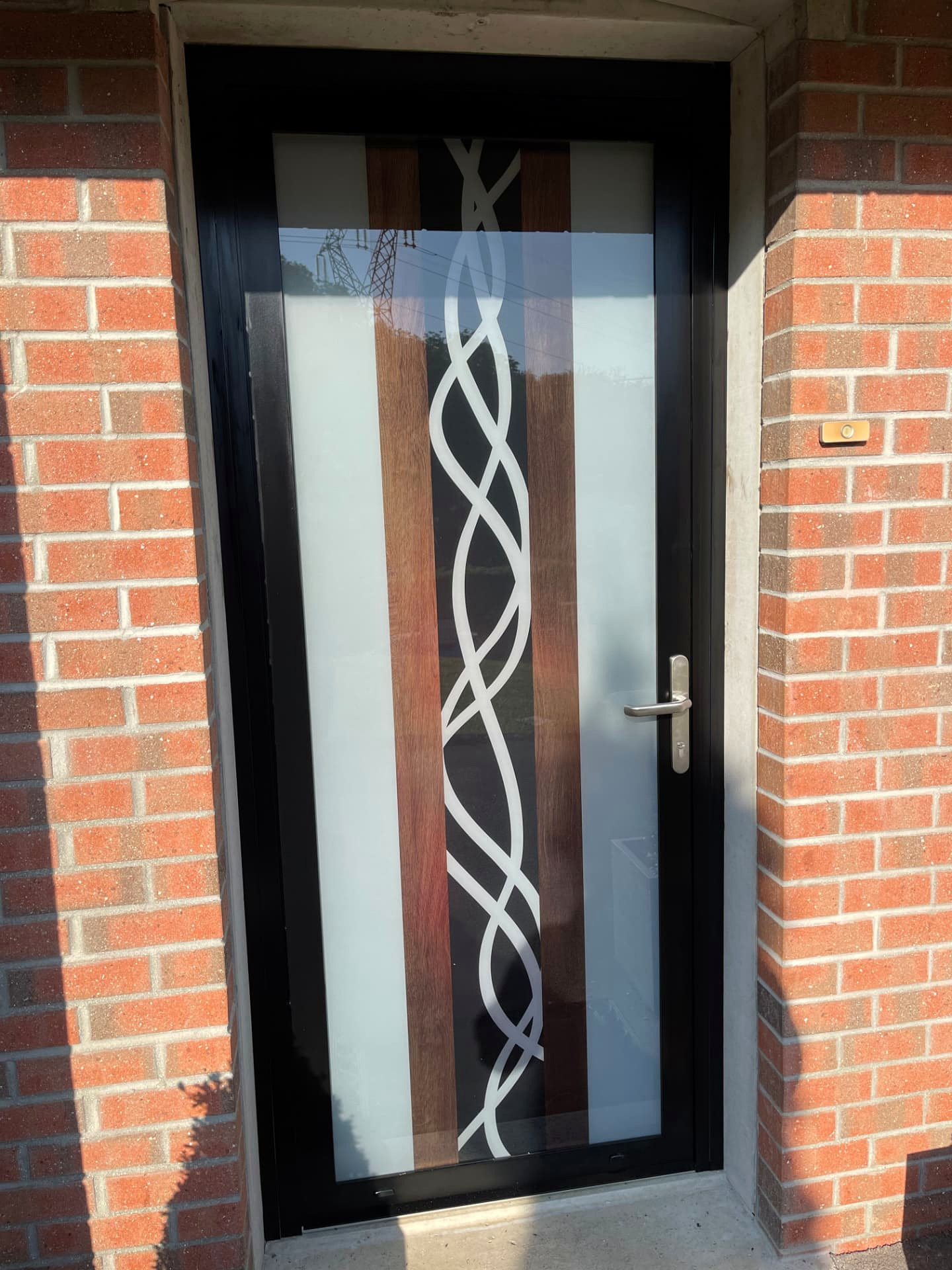 Réalisation VITREC d'une porte d'entrée GraphiDéco vitrée avec lignes blanches entrelacées et décor bois