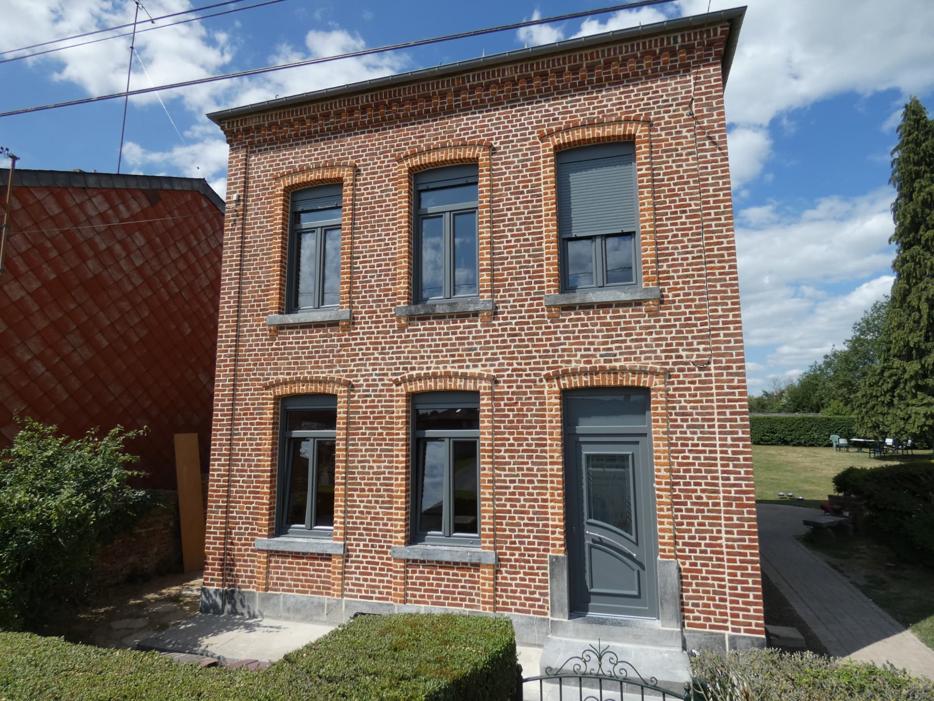 Maison en brique avec fenêtres PVC gris, volets roulants et porte assortie